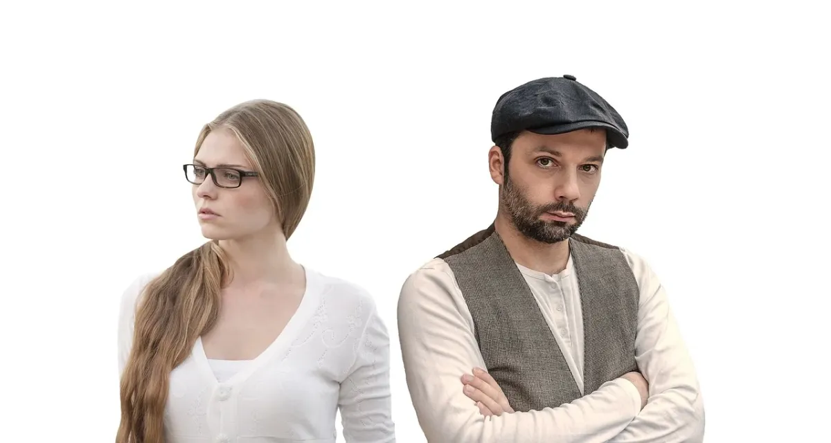 Dwie obrączki leżące w oddaleniu na drewnianym stole przy migoczącej świecy, symbolizujące dystans w małżeństwie.
